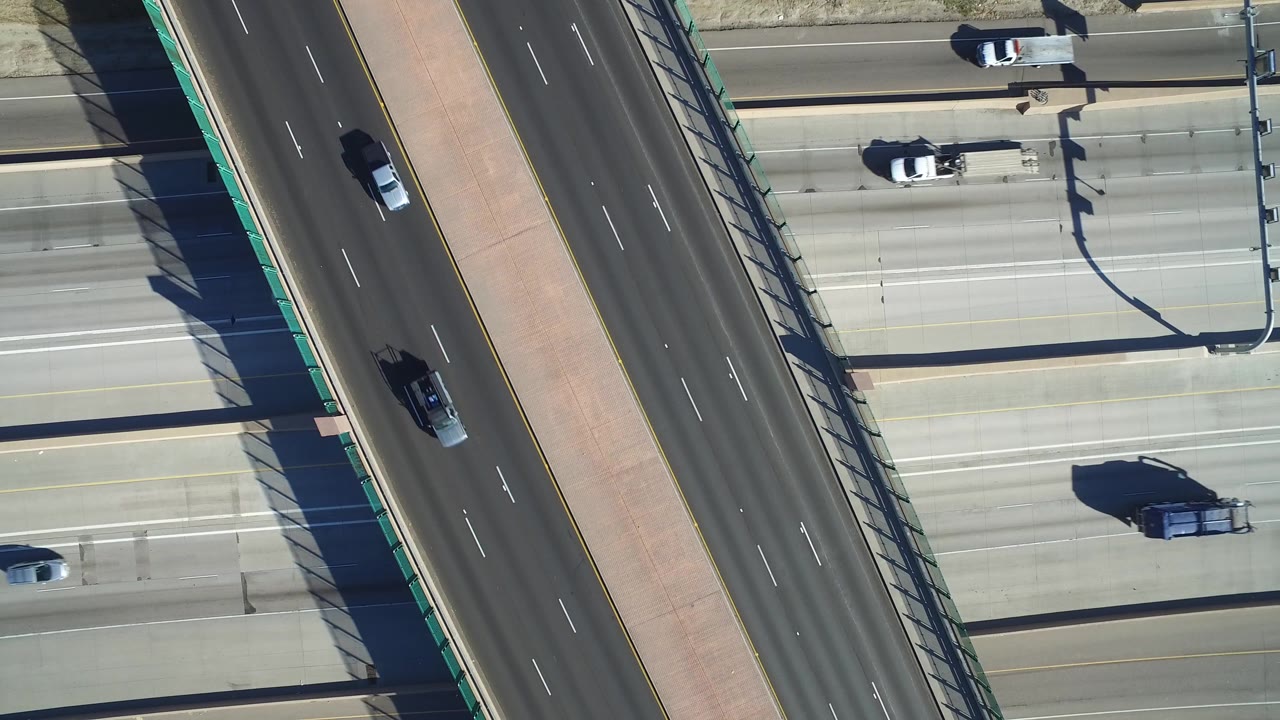 High overhead view in Hidden Lake, Colorado with cars spaced across pale concrete lanes, a darker overpass running diagonally, and no visible people.