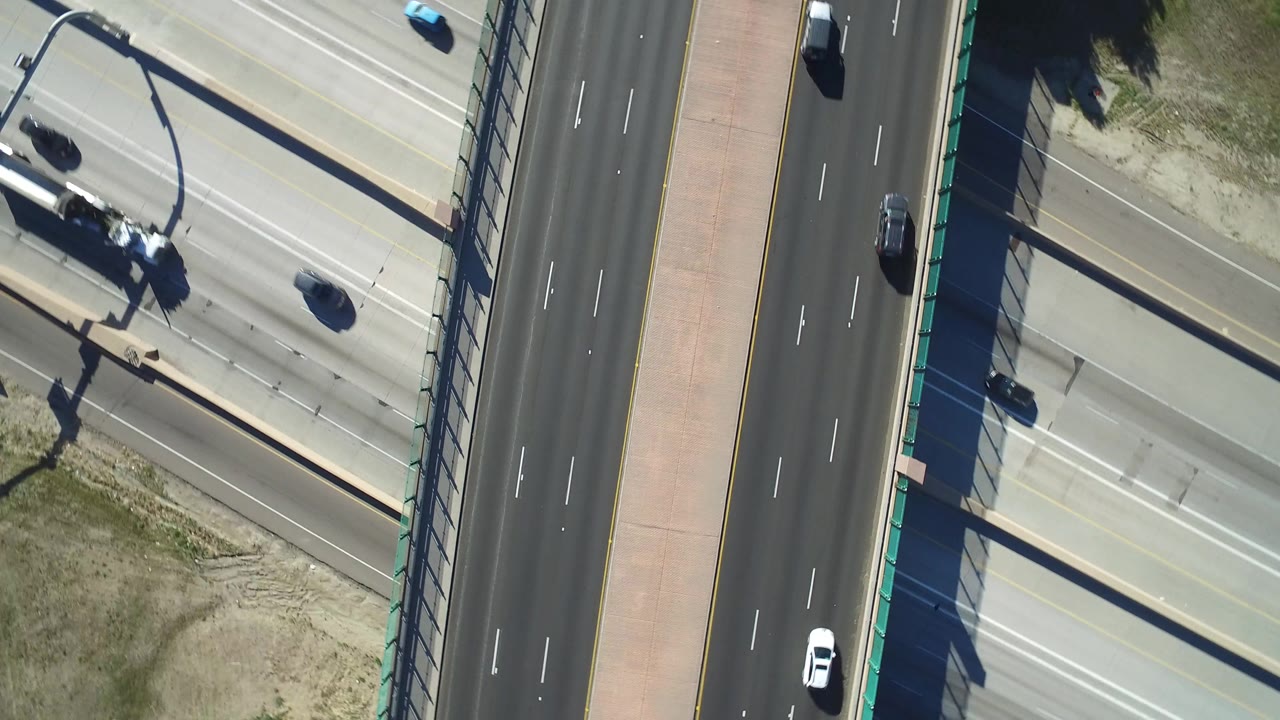 Overhead frame in Hidden Lake, Colorado, with the overpass running vertically through the shot, light traffic on both roads, strong shadows, and no visible people.