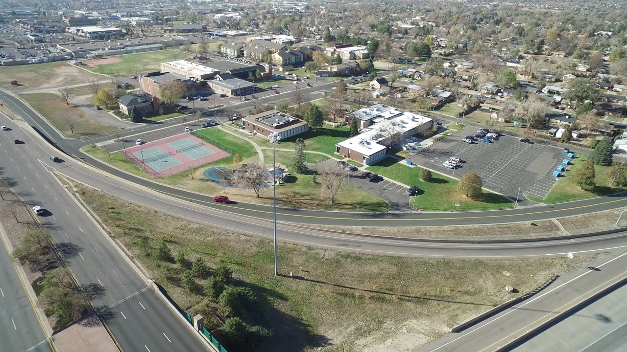 Aerial view of a highway beside tennis courts, parking lots, low buildings, and residential streets.