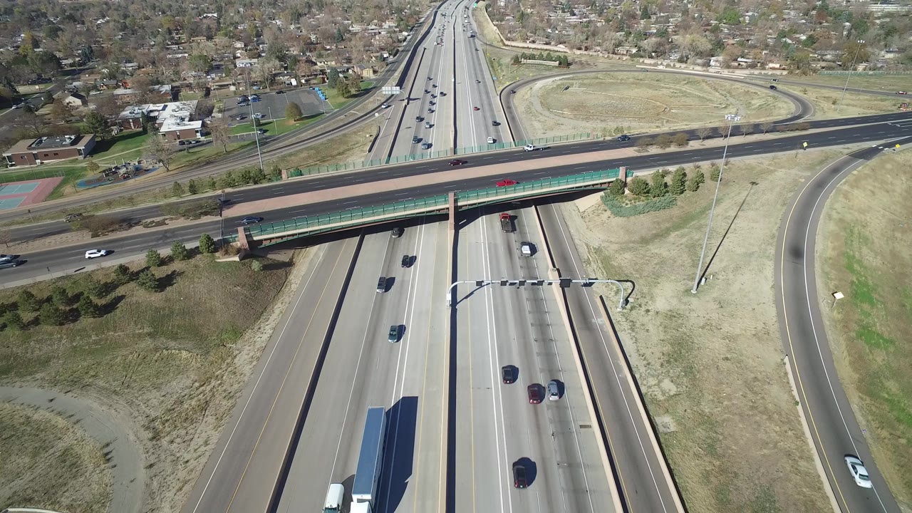 Elevated Hidden Lake, Colorado frame with vehicles on the main highway, a horizontal overpass, looping ramp pavement, dry roadside grass, residential blocks, and no visible people.