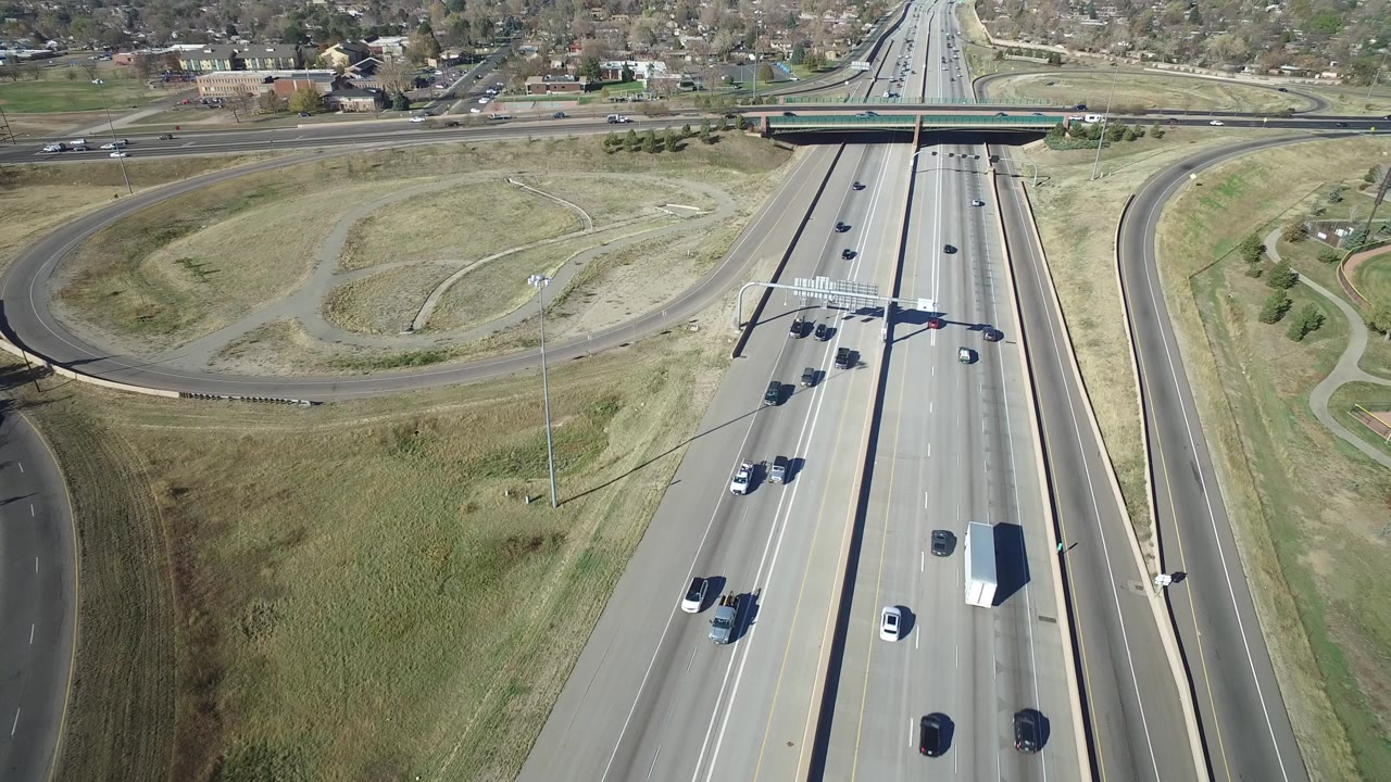 Aerial view of a divided highway with cars, trucks, grass, ramps, and an overpass.