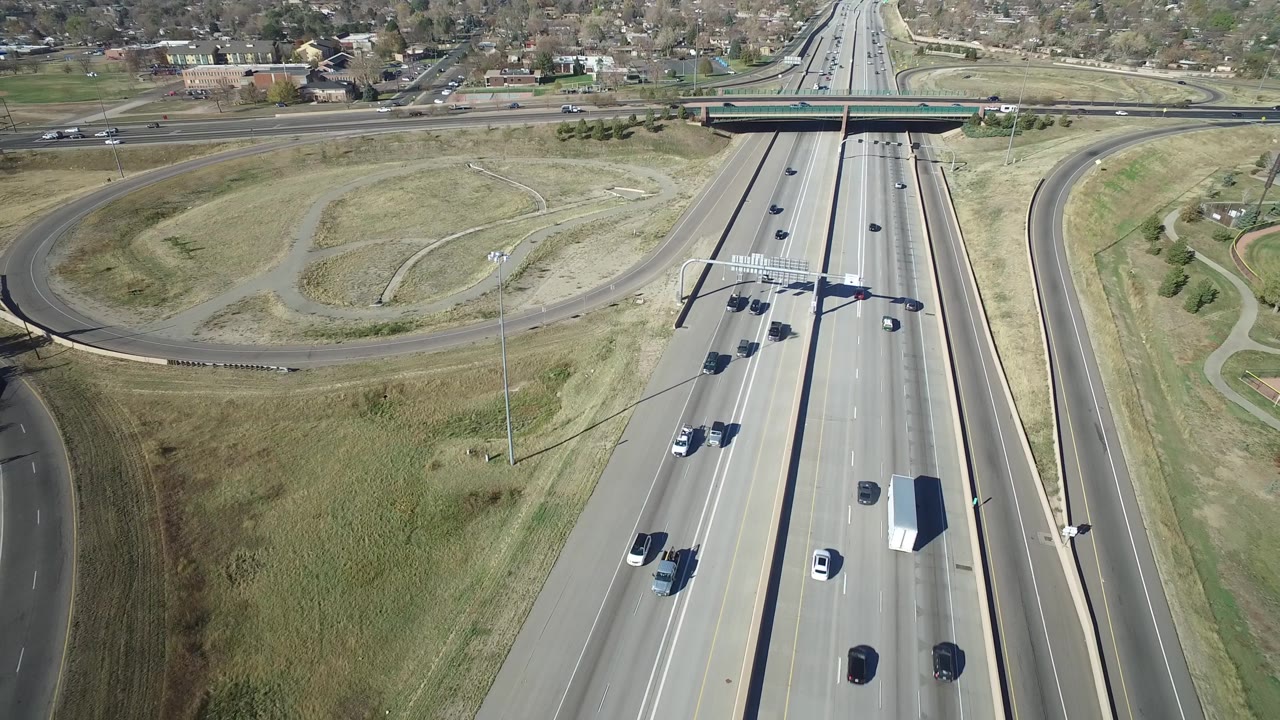 Aerial frame in Hidden Lake, Colorado with the highway still centered, more vehicles spaced across both directions, a curved ramp to the right, and no visible people.