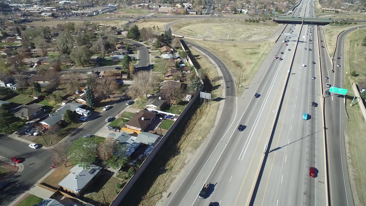 Aerial view in Hidden Lake, Colorado with the roadway centered, cars spaced across the lanes, homes and trees to one side, and no visible people.