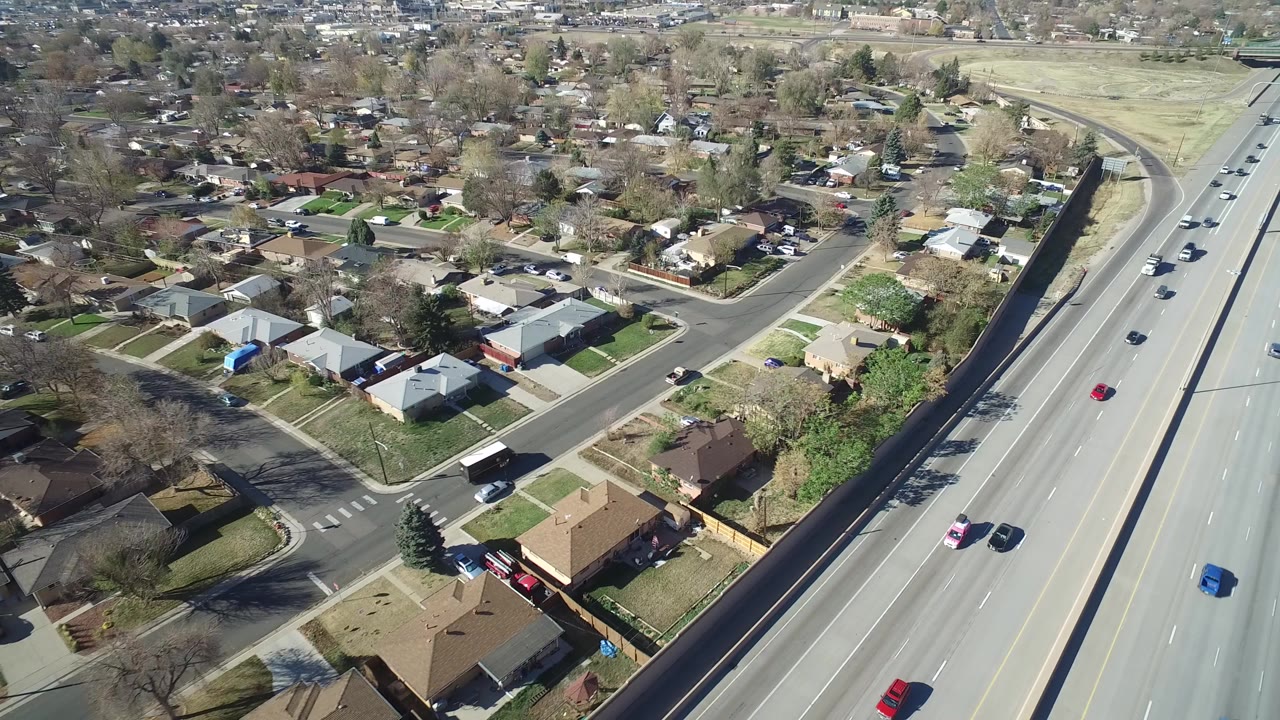 High aerial view in Hidden Lake, Colorado showing a divided highway, nearby single-family homes, side streets, lawns, and no visible people.
