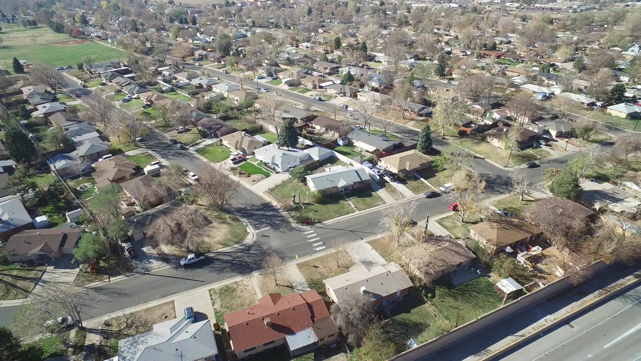 Aerial view of suburban houses, streets, trees, and a road edge.