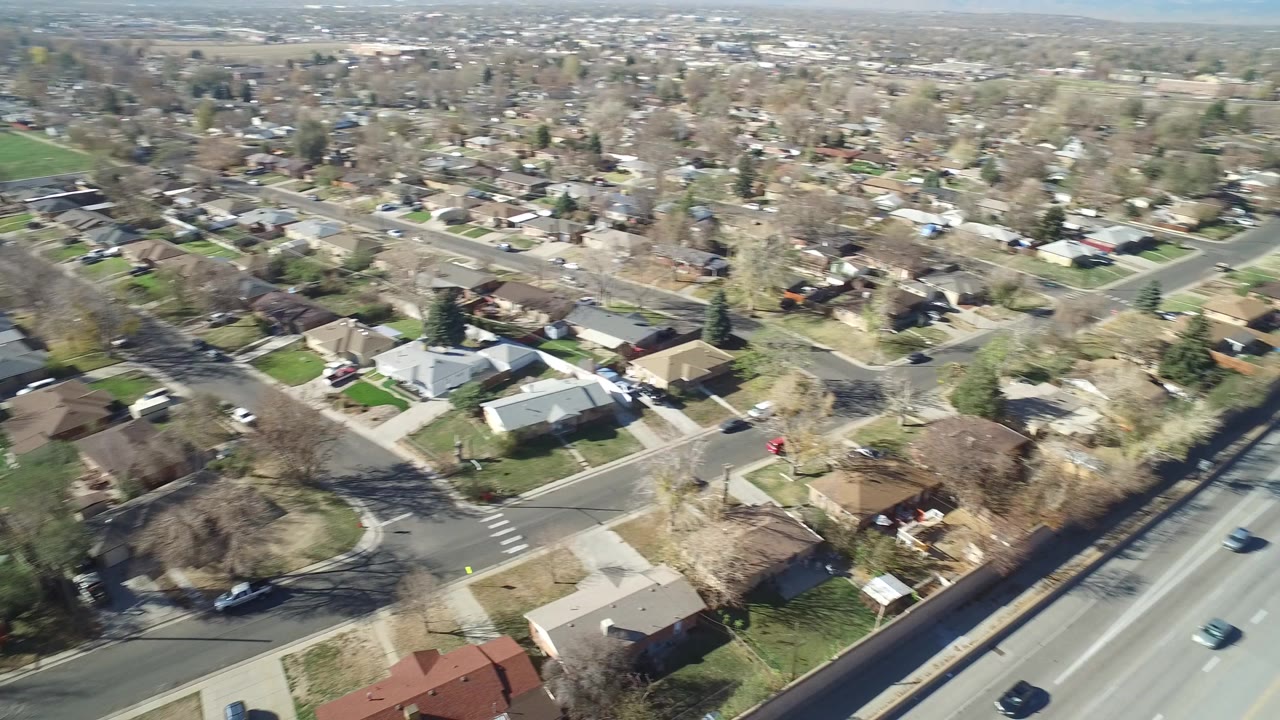 Early frame from Hidden Lake, Colorado showing a high aerial view over residential blocks, a divided road, scattered vehicles, leafless trees, and no visible people.