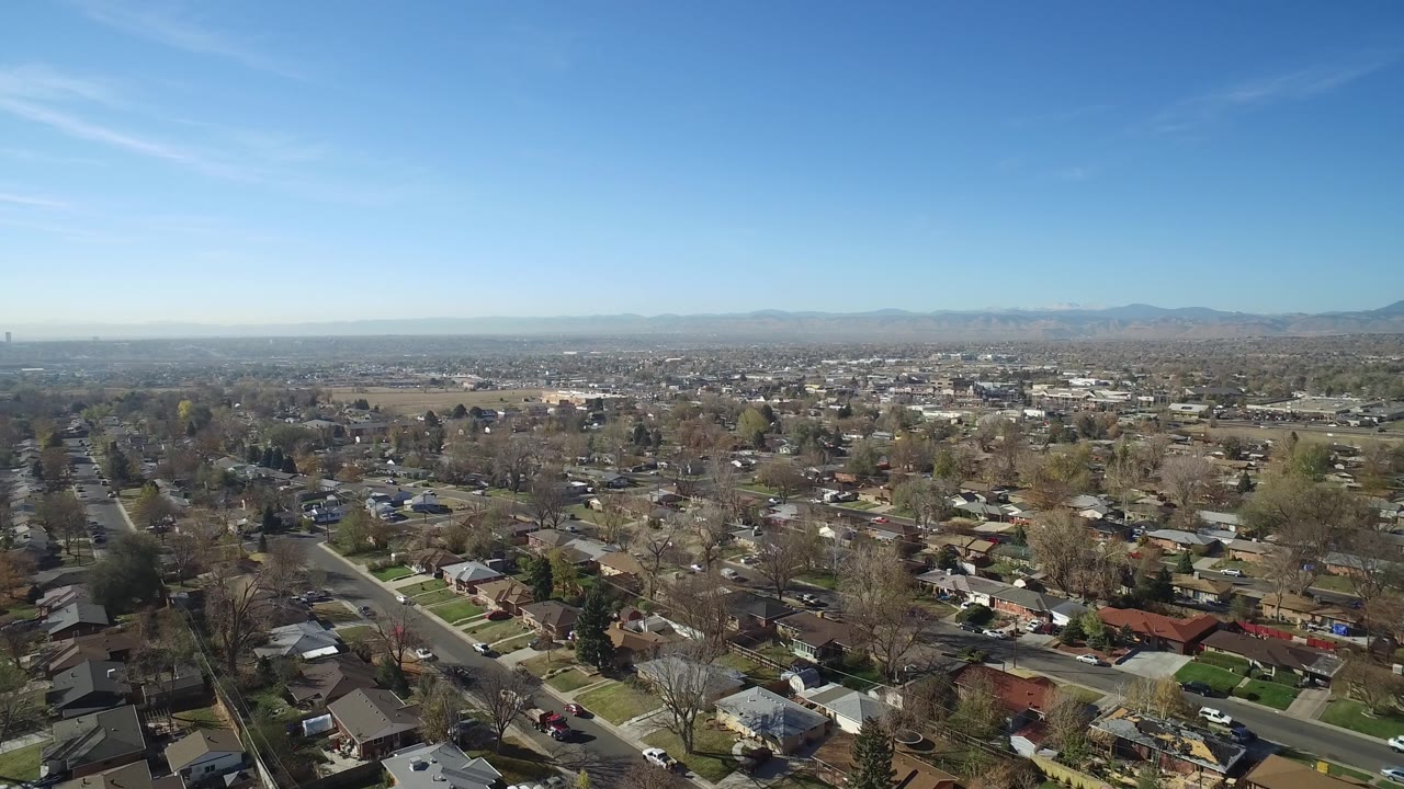 Suburban aerial view with a road, rooftops, trees, and wide horizon