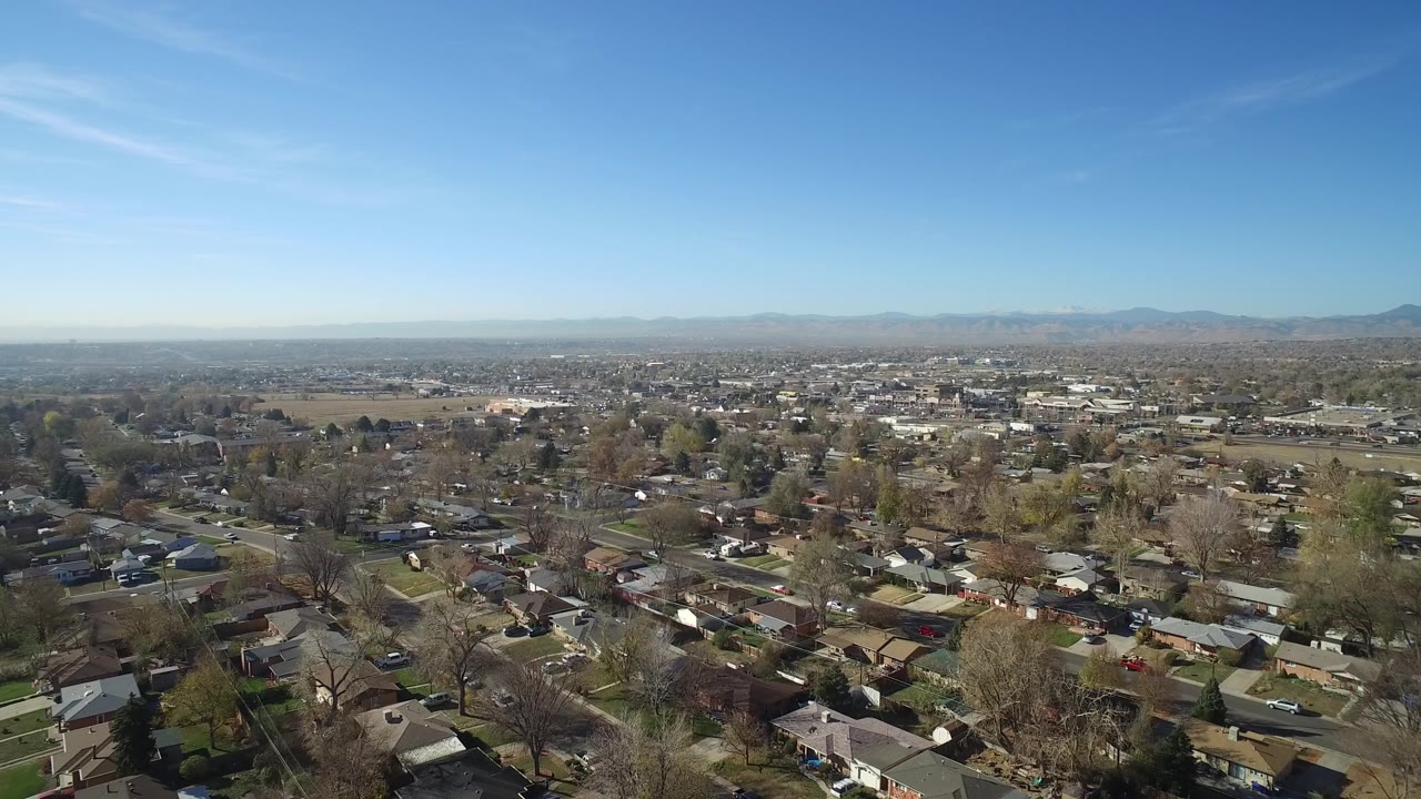 Suburban aerial panorama with houses, leafless trees, roads, open land, and mountains.