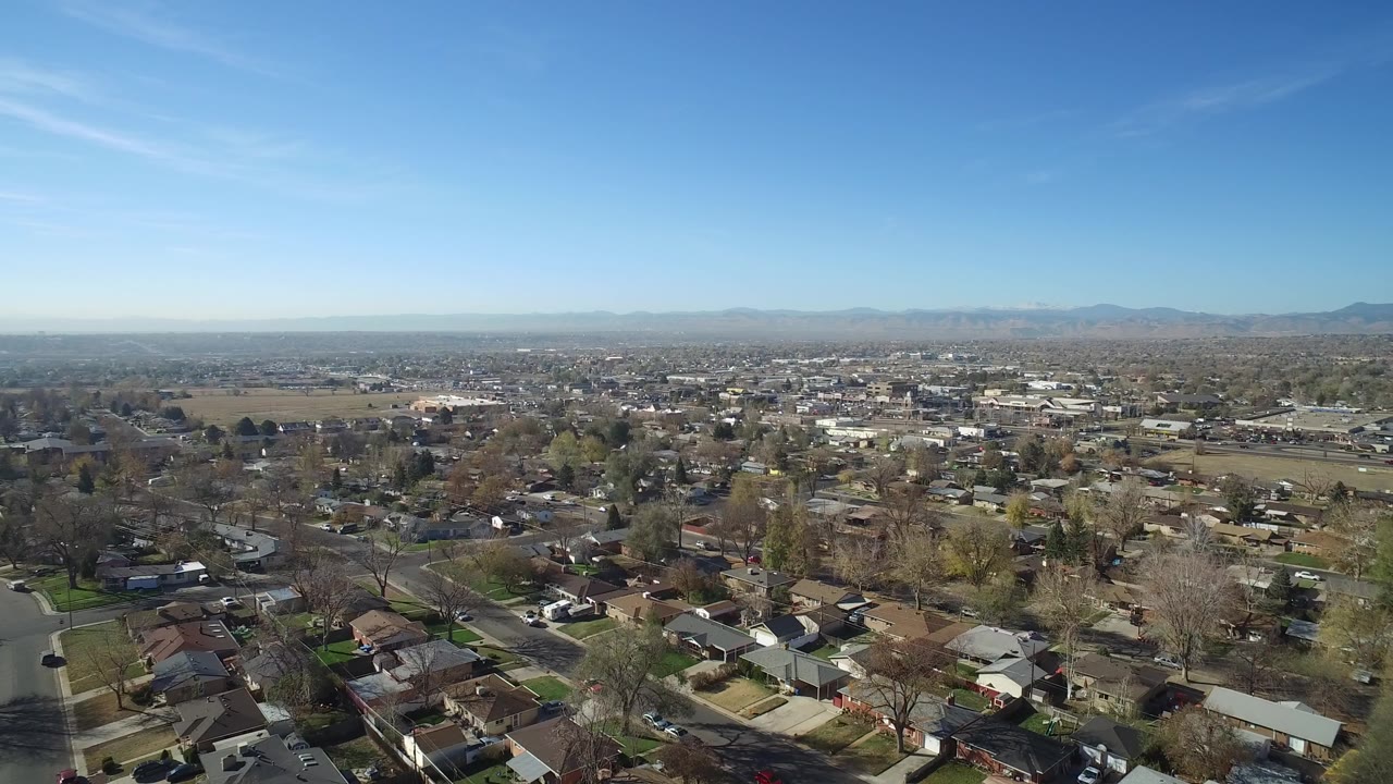 Wide aerial view over suburban rooftops and streets beneath a clear blue sky.