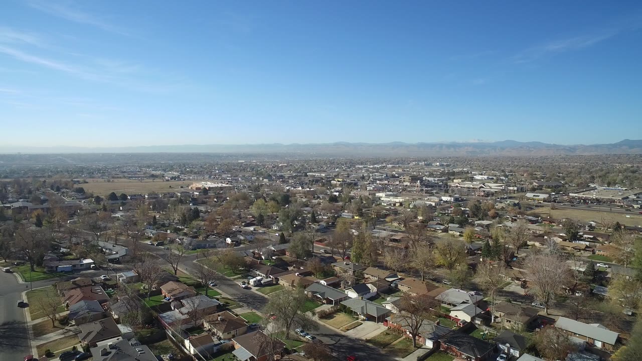 Second frame of Hidden Lake, Colorado showing residential blocks, bare trees, open ground, distant town structures, a pale mountain line, and no visible people.