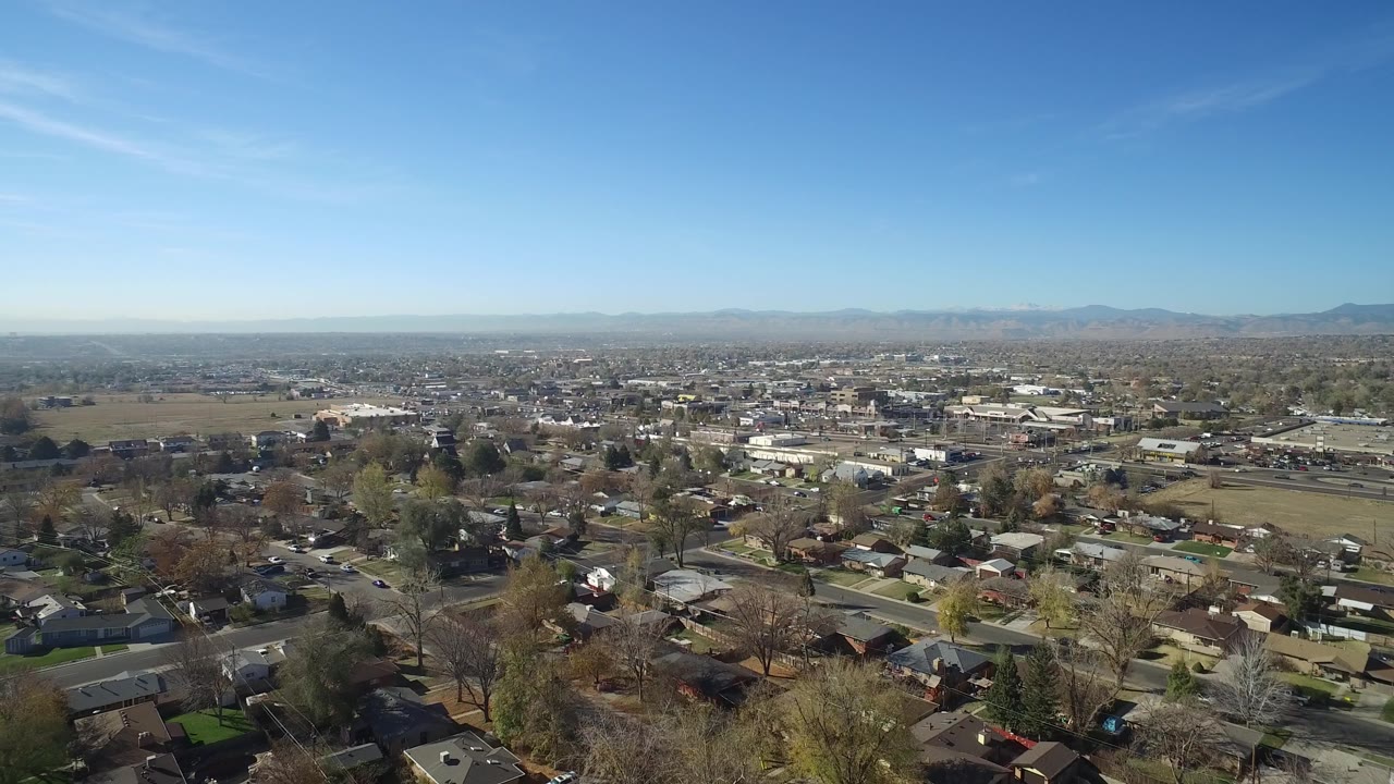 Drone view of a suburban block with houses, roads, fields, and mountains.
