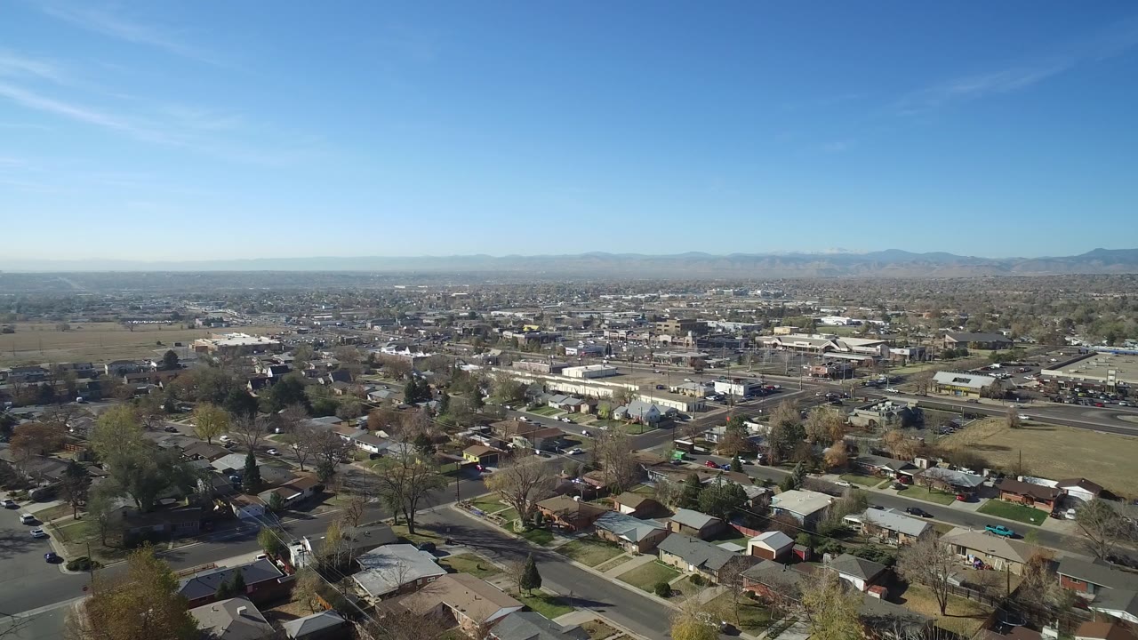 Wide aerial view over homes, streets, fields, and distant mountains.