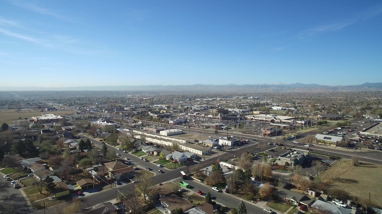 Aerial view over suburban homes, roads, and distant mountains under blue sky.