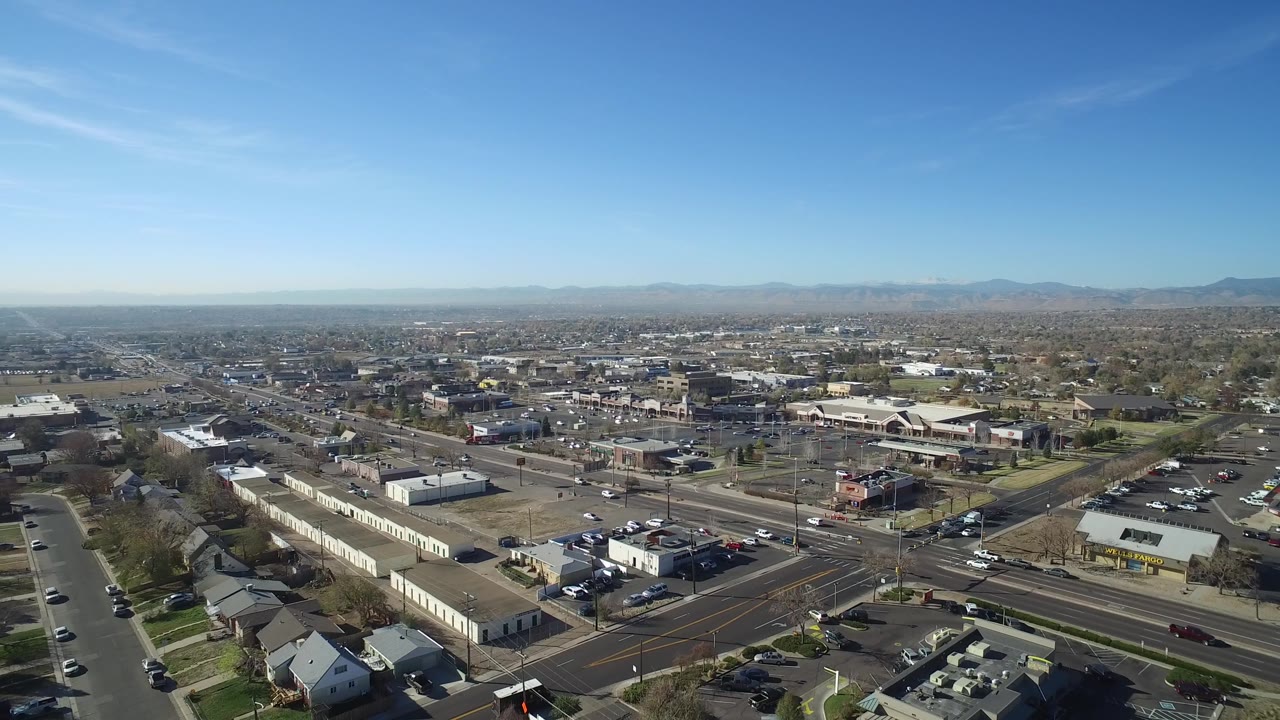 Aerial frame in Hidden Lake, Colorado, looking across a main road and retail blocks toward a hazy mountain horizon, with no visible people.