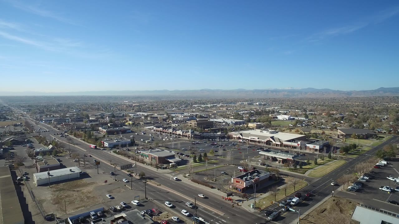 Aerial view over roads, parking lots, and low commercial buildings under a blue sky.