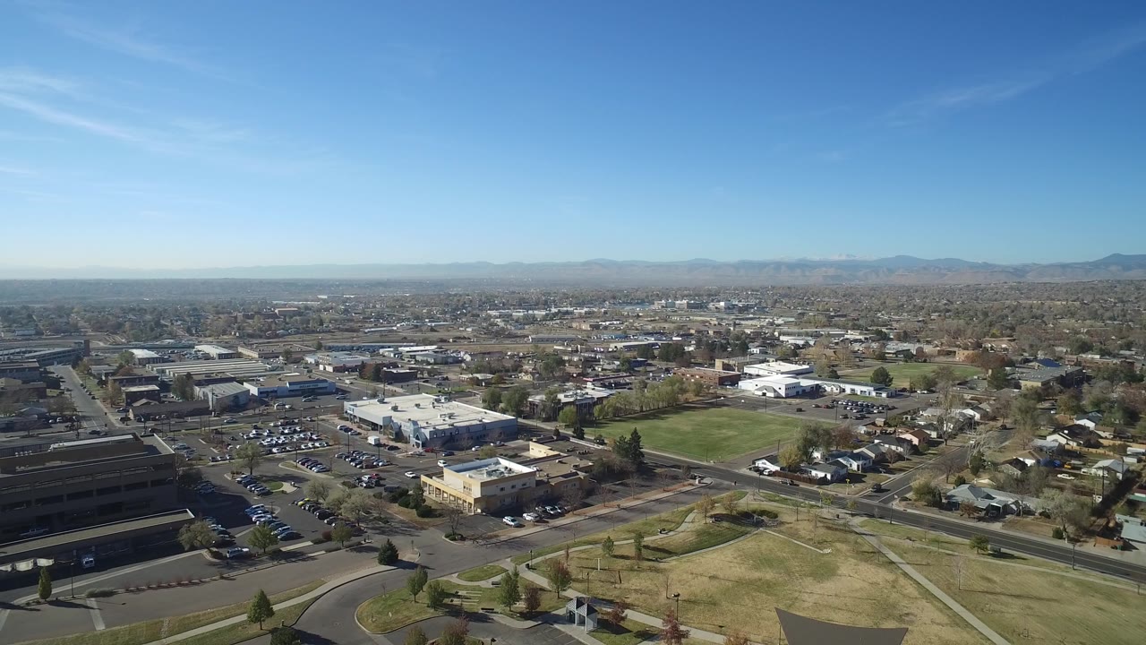 High aerial view over roads, parking lots, homes, fields, and distant mountains.