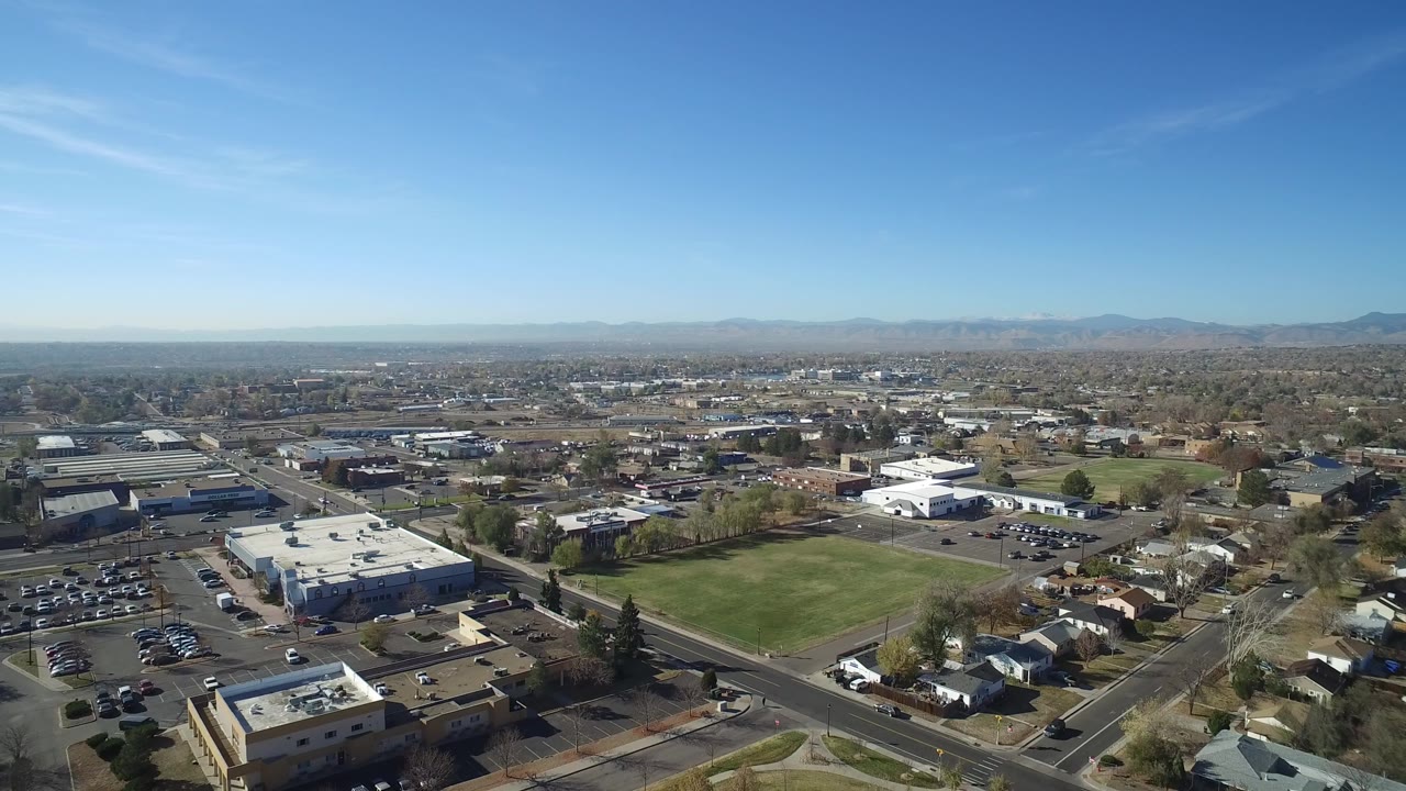 Wide aerial view over roads, buildings, lawns, and distant mountains under a blue sky.