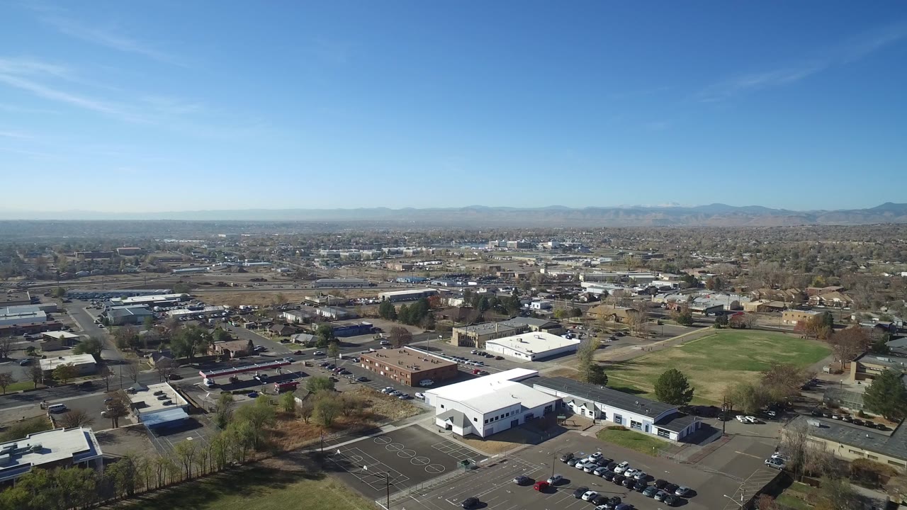 Second frame of the Hidden Lake, Colorado aerial, with the white buildings slightly more centered, the grass field to the right, rows of homes beyond, and no visible people.