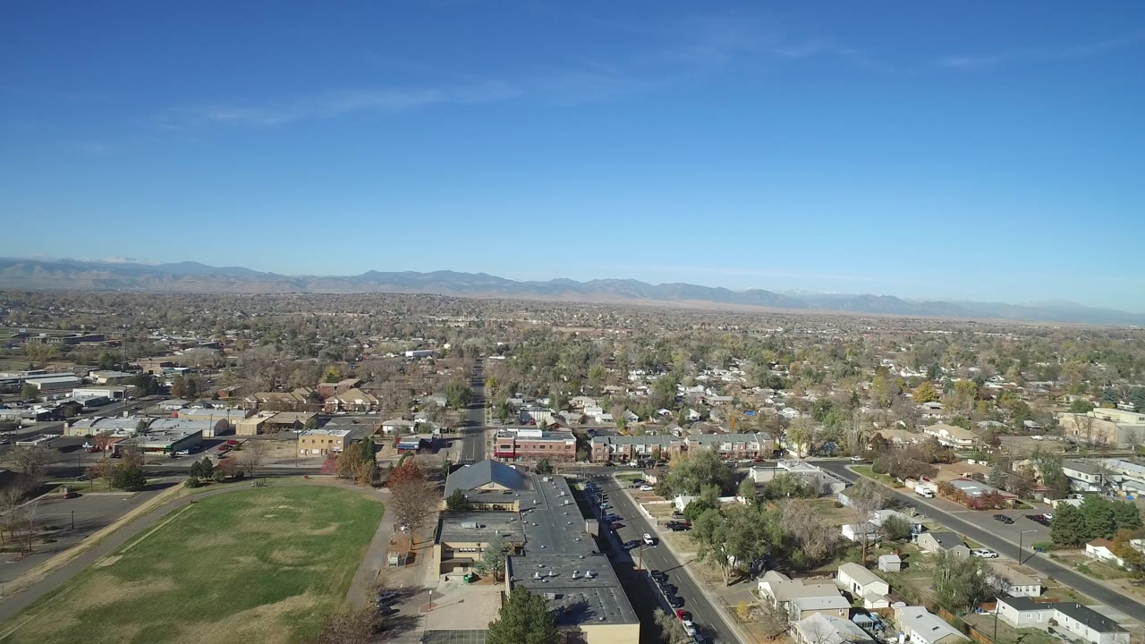 Aerial view over suburban streets and a large grass field under a blue sky.
