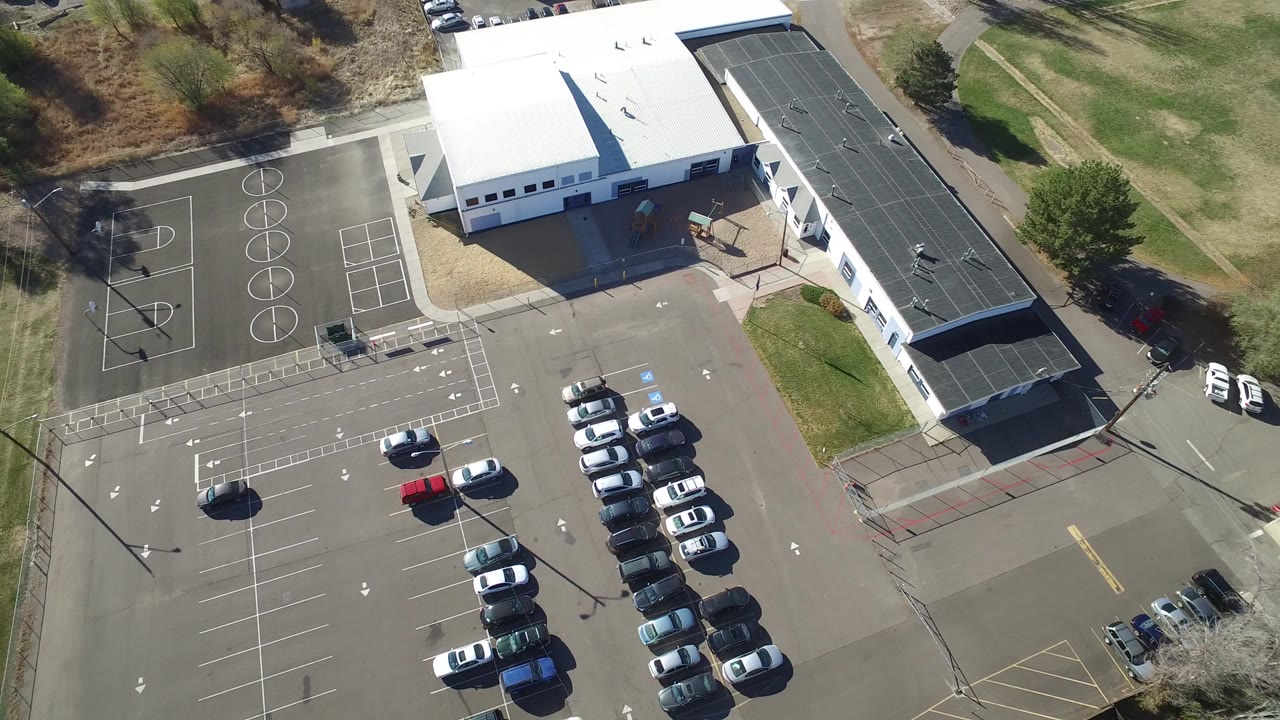 Aerial view of a white-roofed building beside courts and a full parking lot.
