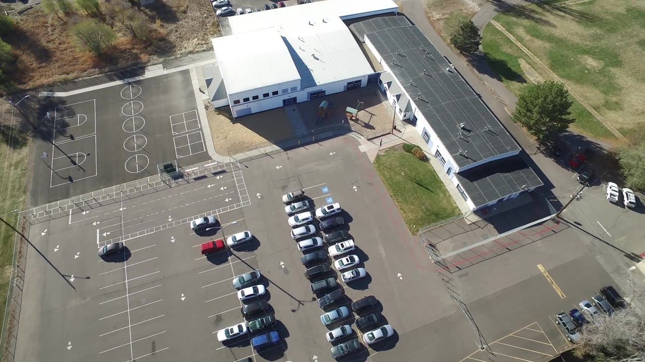 Second aerial frame in Hidden Lake, Colorado with the long dark roof more centered, rows of parked cars below it, basketball court markings at left, and no visible people.