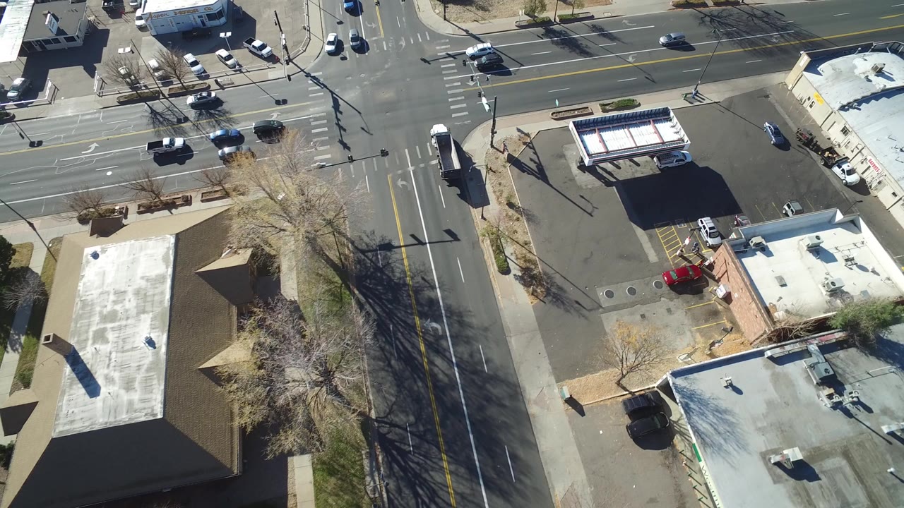 Aerial view of a sunlit intersection beside commercial rooftops and parking lots.