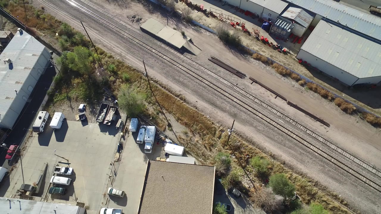 Overhead view of railroad tracks beside warehouses and parked work vehicles.