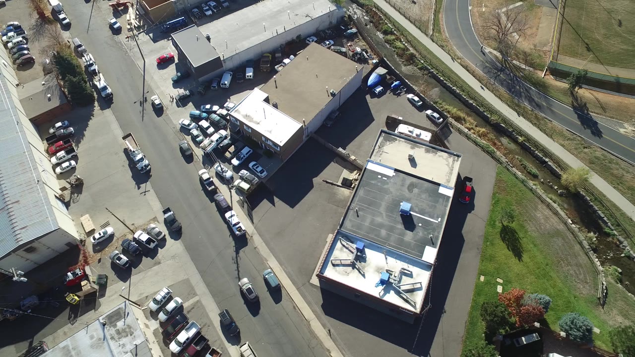 Aerial view of small buildings, parked cars, and a road beside grass