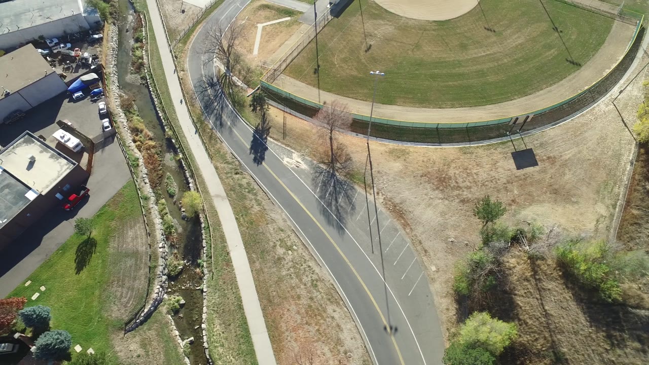 Top-down view of a curved road, fenced grass field, dry ground, and trees.