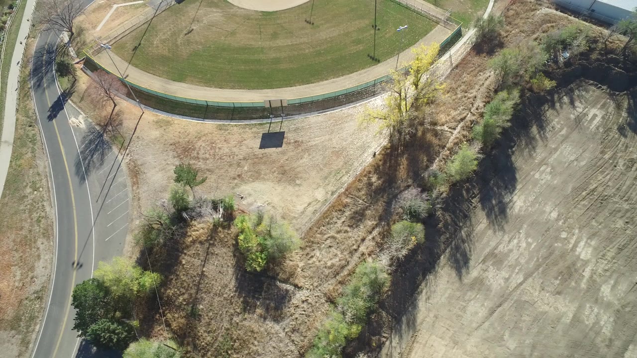 Aerial view of curved road, fenced lawn, brush, and dry open ground.