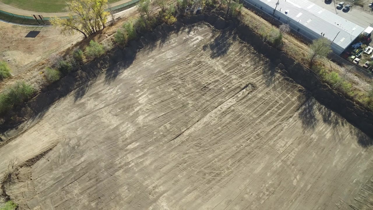 Aerial view of a plowed field bordered by trees and a light-roofed building.