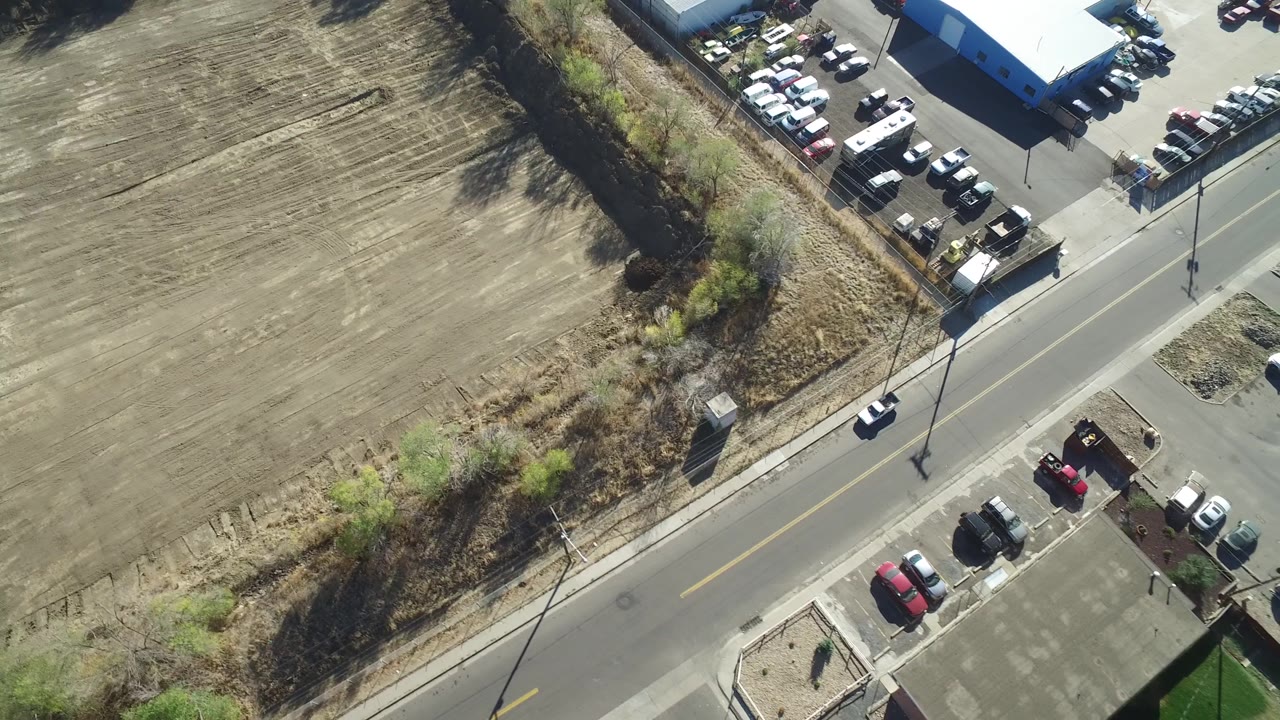 Aerial frame in Hidden Lake, Colorado looking down on the same road, with open brown land on one side, parked cars near buildings on both sides, and no visible people.