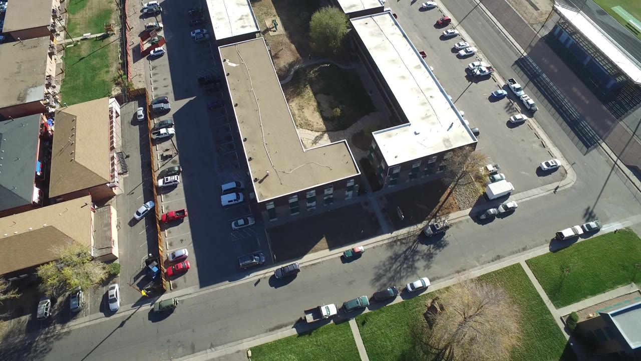 Top-down street corner with apartment buildings and parked vehicles.