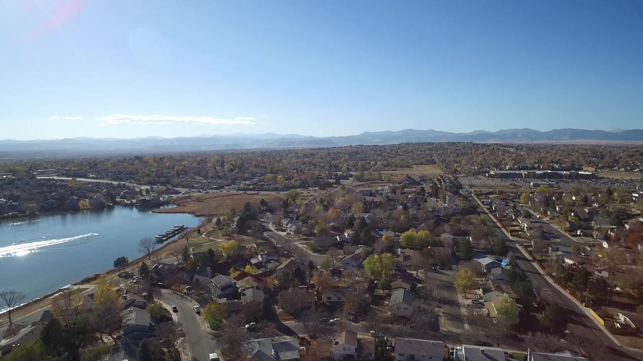 Aerial view over Hidden Lake, Colorado with the lake on the left, homes and curving streets in the foreground, distant mountains on the horizon, and no visible people.