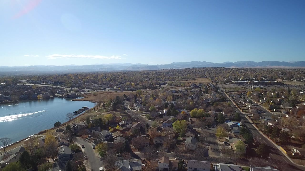 Hidden Lake, Colorado aerial frame showing more of the lakeshore at left, a bright white wake on the water, residential roofs below, and no visible people.