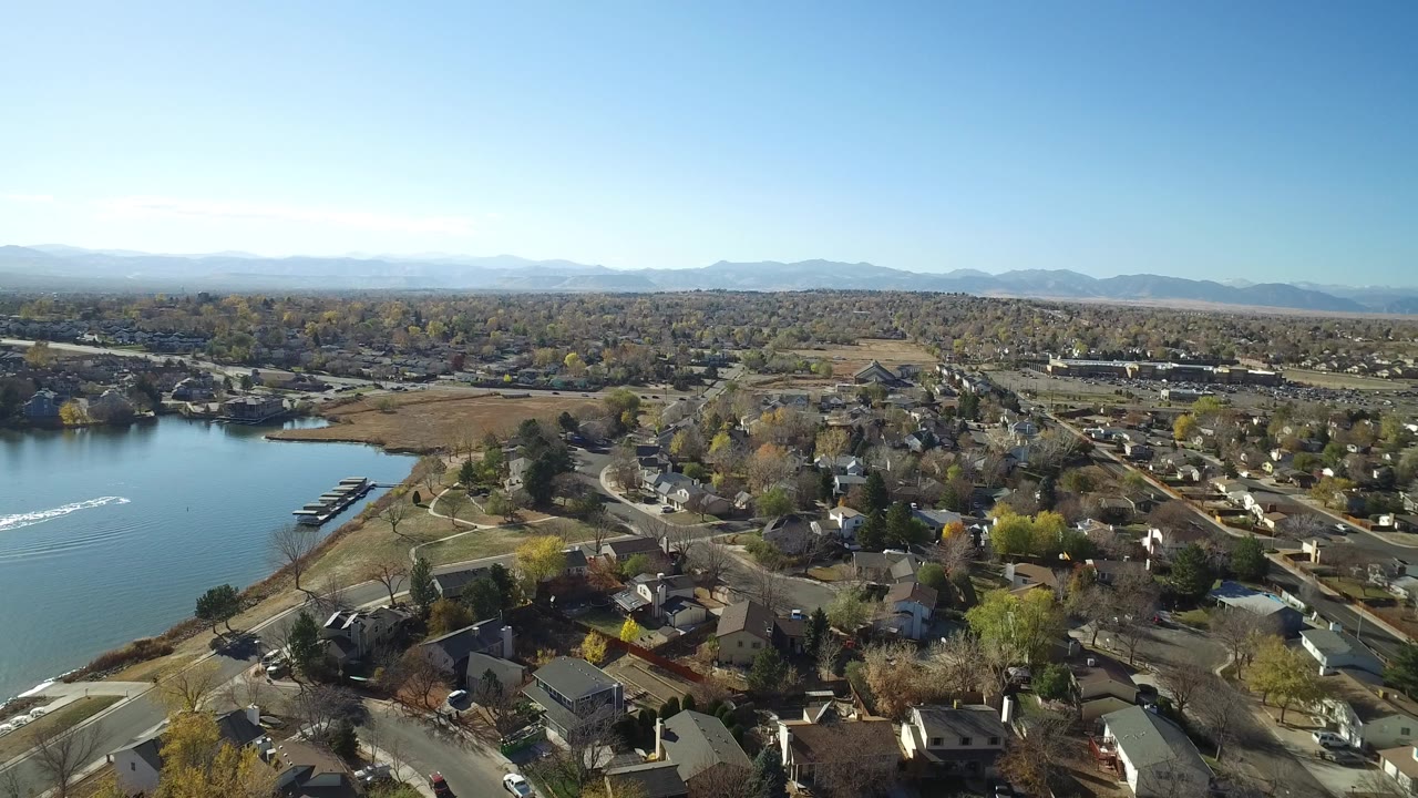 Aerial view over Hidden Lake, Colorado with a blue lake at left, residential streets and homes below, autumn trees across the neighborhood, distant mountains, and no visible people.