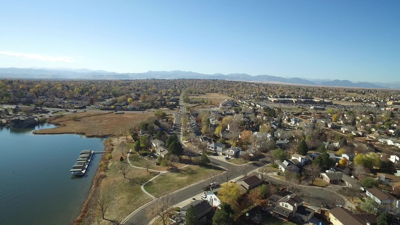 Aerial view of lake docks, shoreline parkland, roads, houses, and distant mountains.