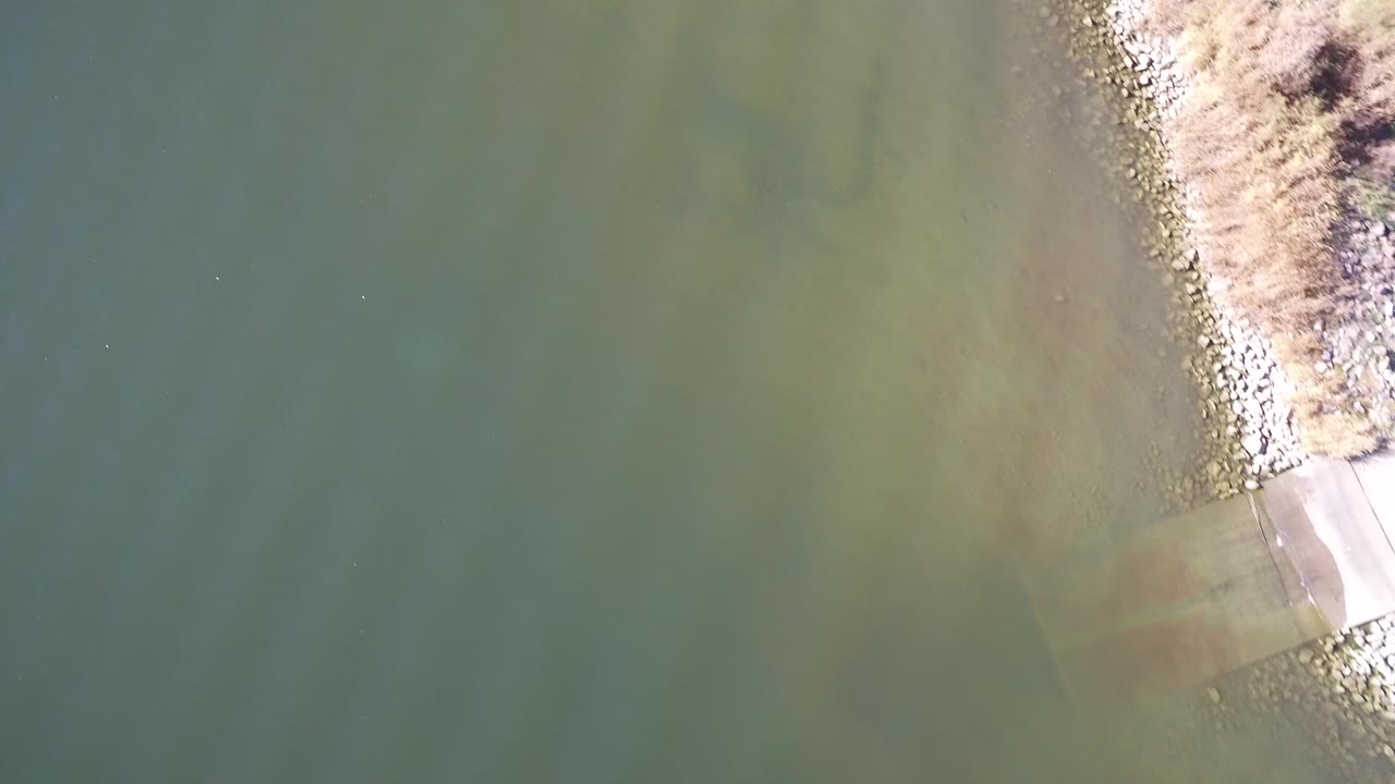Overhead green lake water beside a rocky shoreline and small concrete edge.