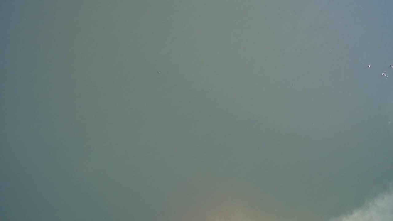 Overhead Hidden Lake, Colorado frame with a brighter white drift along the lower edge, open green-gray surface above it, scattered small white specks, and no visible people.