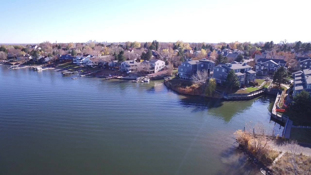 Aerial frame over Hidden Lake, Colorado showing calm water in the foreground, large homes along the shore, docks, bare trees, and no visible people.