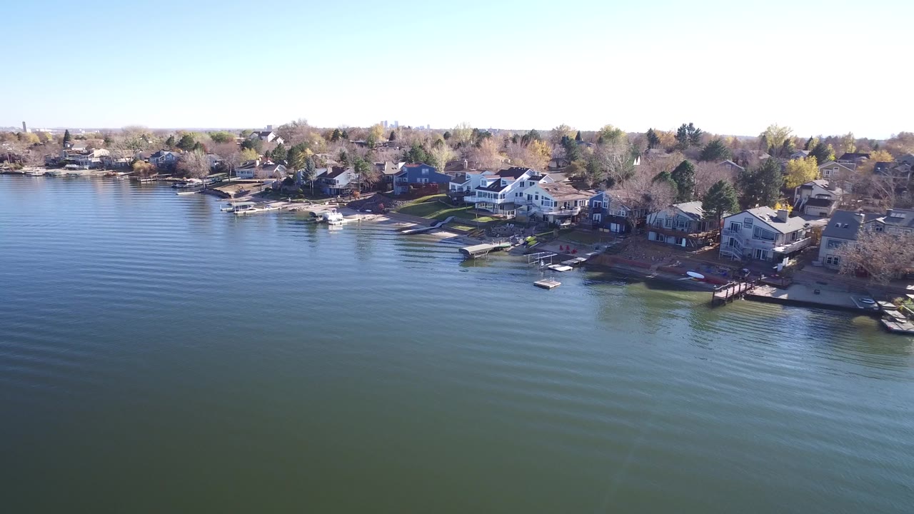 Drone view across lake water toward a shoreline neighborhood.