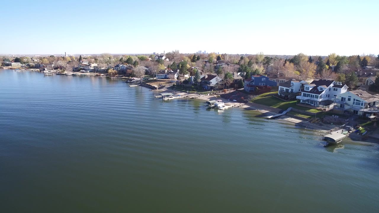 Aerial view over lake water toward shoreline homes and docks