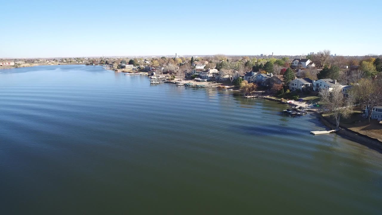 Aerial view over lake water toward shoreline homes and docks.