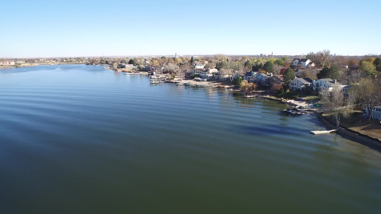 Aerial view of Hidden Lake, Colorado with rippled water across the foreground, a line of houses and docks on the right shoreline, sparse trees, and no visible people.