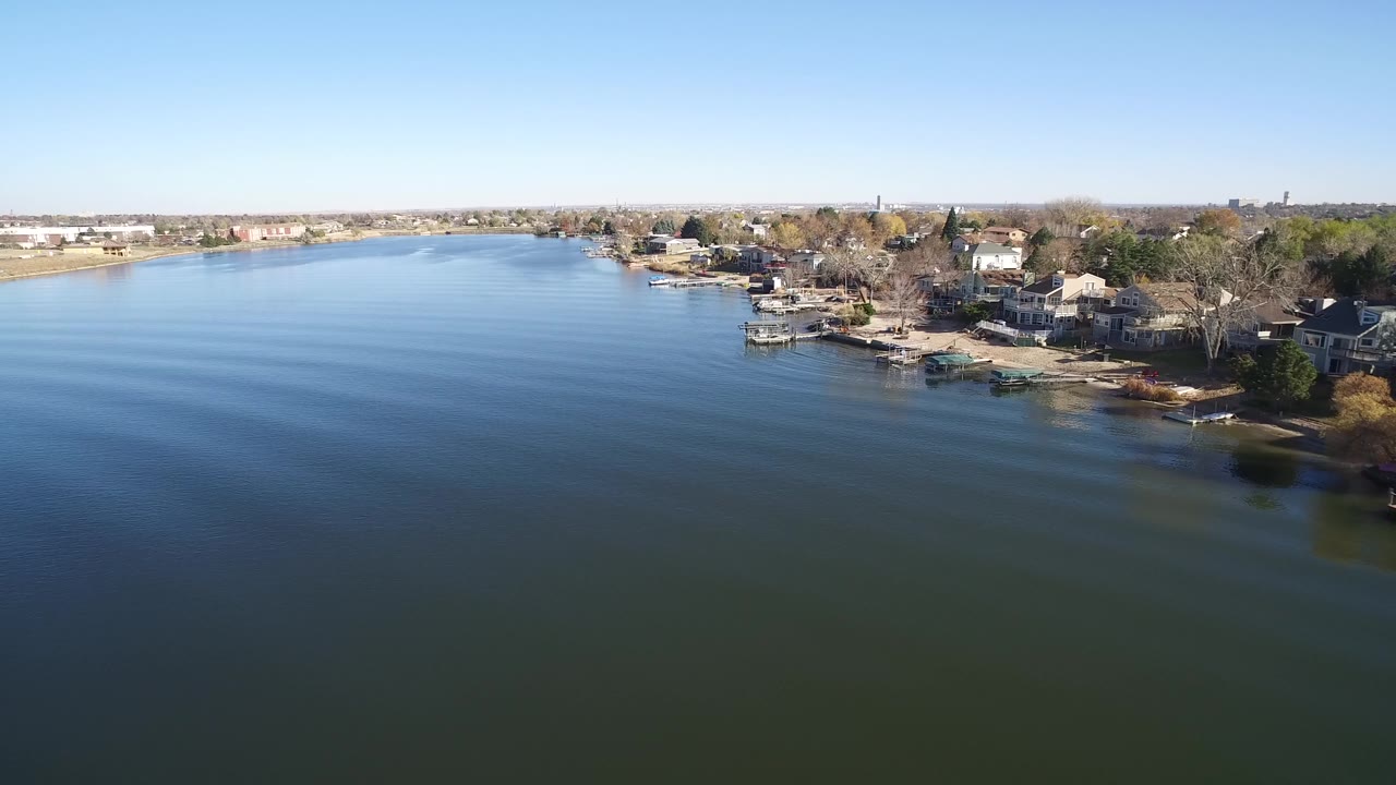 Drone view of calm lake water beside a developed residential shoreline.