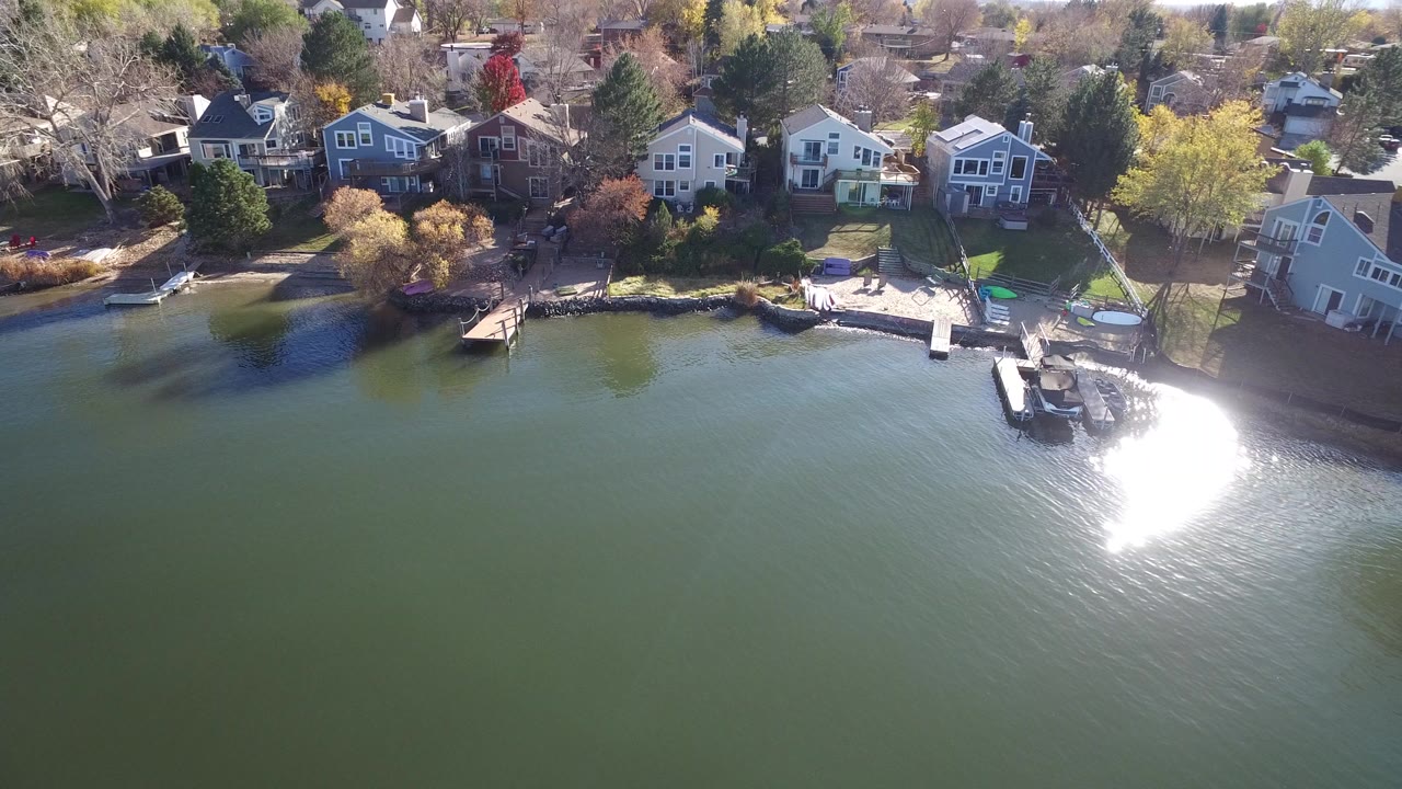 Aerial view of lakefront houses, docks, boats, and sun glare on green water.