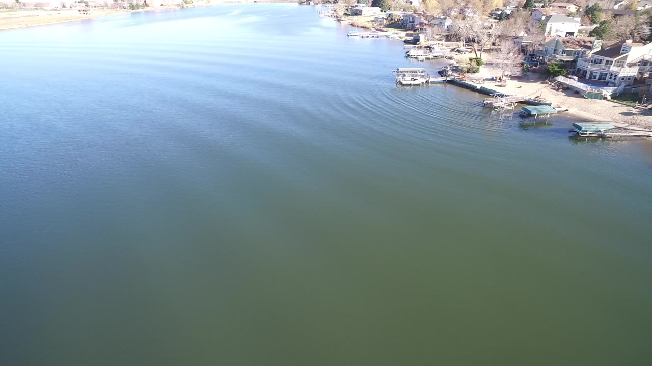 Aerial view of blue-green lake water beside a residential shoreline with docks.