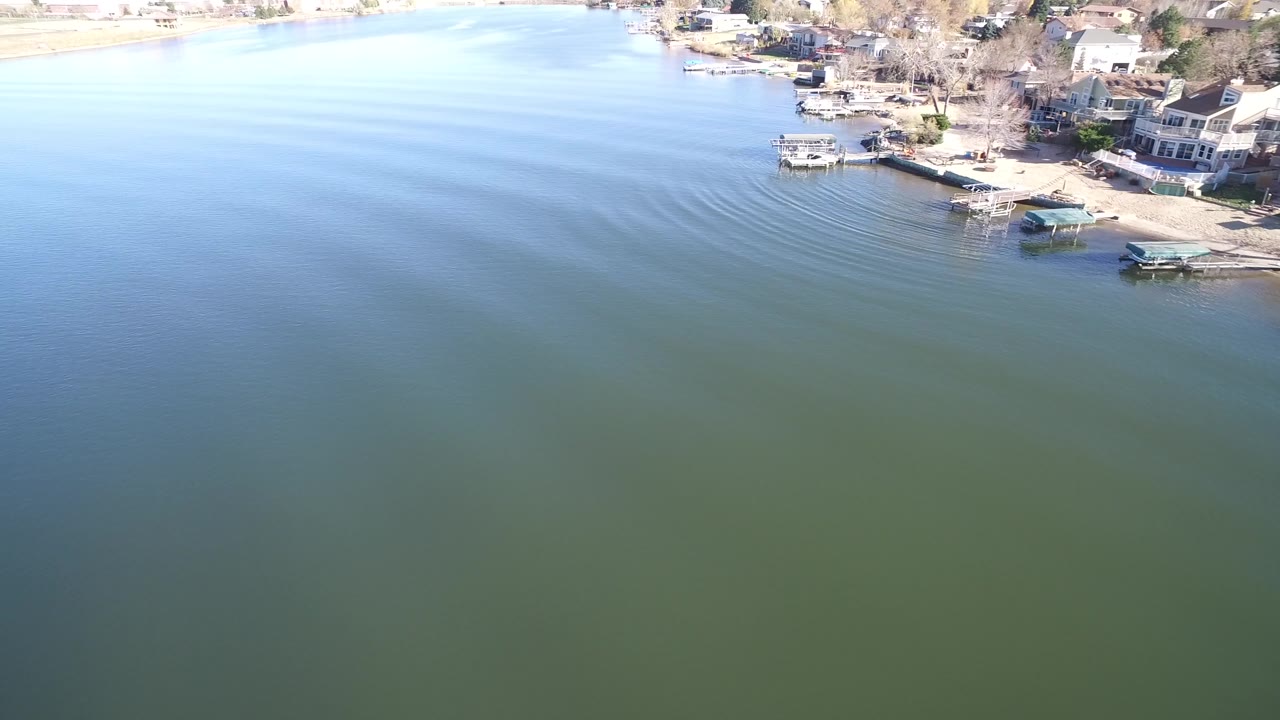 Aerial view of Hidden Lake, Colorado showing broad blue water, curved ripple lines near the shoreline, lakeside houses, docks, and no visible people.