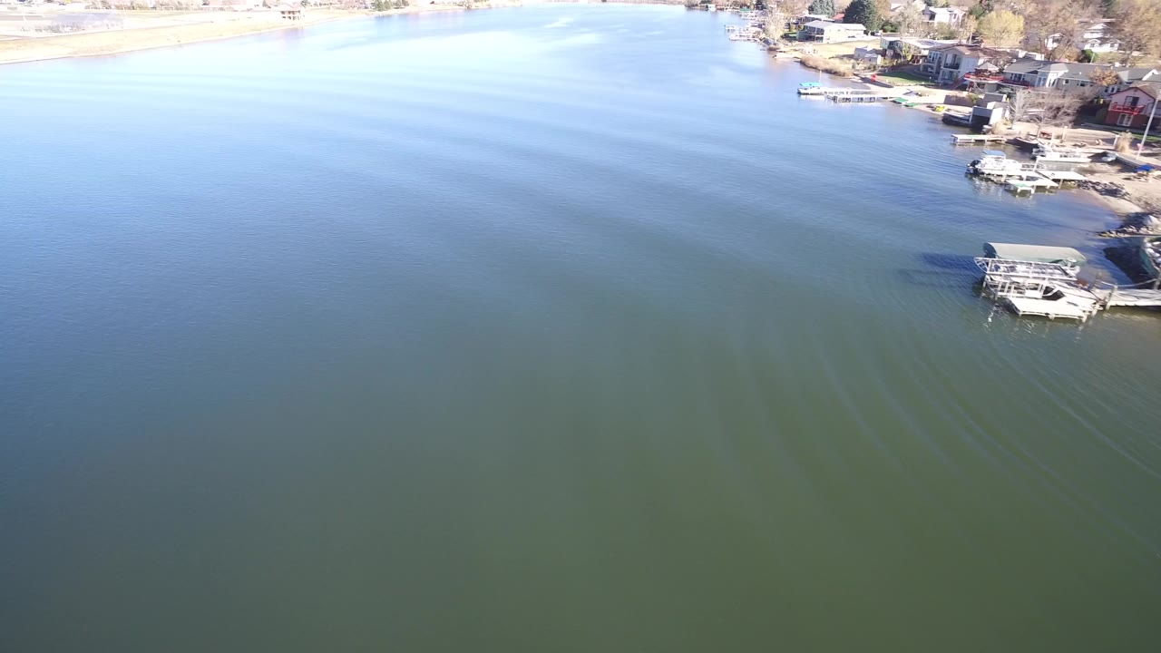Aerial view of Hidden Lake, Colorado, looking across rippled green-blue water toward docks, boats, and shoreline homes, with no visible people.