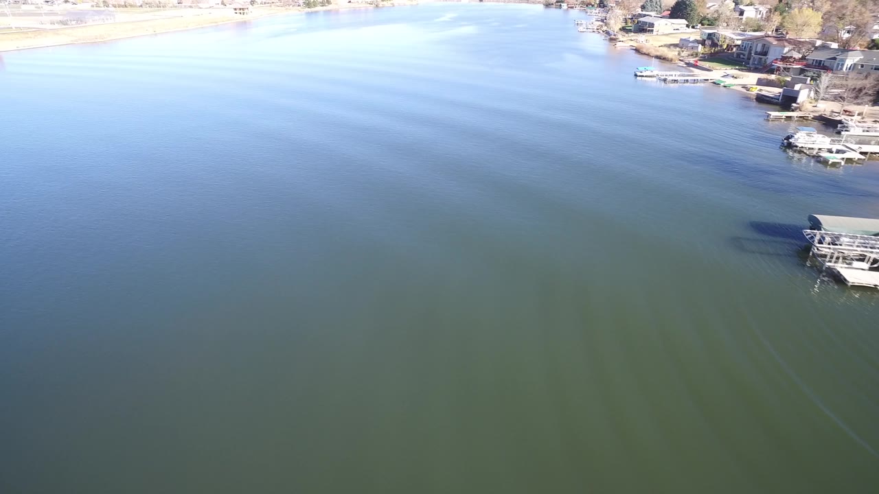 Lake water with faint wake lines, a partial docked boat, and bright shoreline near the top.